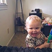 Mara is registered to the contest to win money with this photo: toddler, child, toy, smiling, blonde_hair, curly_hair, indoor, carpet, lamp, furniture, stuffed_animals, basket, window, shirt, patterned_clothing, happy, person, playful, room, home
