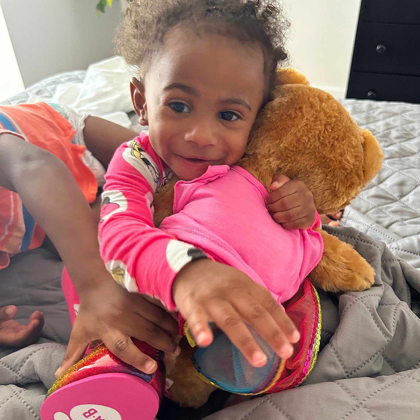 Pheobe joined the competition — help win amazing prizes! bed, blanket, child, colorful, curly_hair, dresser, face, footwear, furniture, hand, indoor, pajamas, person, plant, playful, plush, smile, teddy_bear, toddler, toy