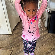 Pheobe joined the competition — help win amazing prizes! arms_raised, child, curly_hair, girl, happy, indoor, kitchen, patterned_clothing, pink_shirt, playful, portrait, purple_shoes, refrigerator, smiling, sneakers, standing, toddler, trash_can, unicorn, wood_floor