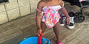 Pheobe is registered to the contest to win money with this photo: toddler, child, smiling, bucket, shovel, sand, swimsuit, pink_shoe, floor, stroller, sneakers, wall, play, happy, outdoor, person, baby, toy, summer, cute