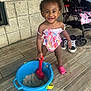 toddler, child, smiling, bucket, shovel, sand, swimsuit, pink_shoe, floor, stroller, sneakers, wall, play, happy, outdoor, person, baby, toy, summer, cute