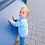 toddler, child, boy, blue_eyes, blond_hair, striped_shirt, jeans, sandals, sidewalk, pavement, greenery, curious, outdoor, urban, window_reflection, standing, hands_on_surface, casual_clothing, daylight, young_child