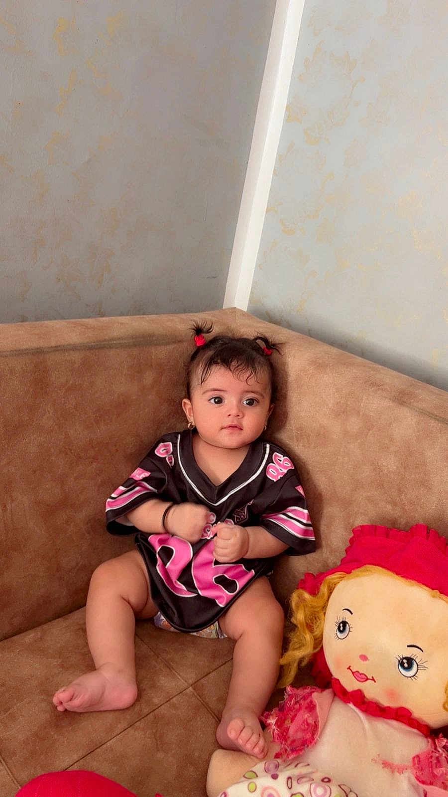 Céline participe au concours pour gagner de l'argent avec cette photo : baby, brown_furniture, casual_clothing, child, comfort, couch, curly_hair, cute, expression, home, indoor, infant, jersey, person, pigtails, playful, plush_doll, portrait, sitting, toy