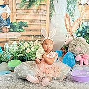 Zaiori is registered to the contest to win money with this photo: baby, child, pink_dress, bunny_ears, plush_toy, easter_eggs, flowers, cushion, carpet, indoor, decorations, celebration, spring, cute, portrait, sitting, person, holiday, festive, soft_toys
