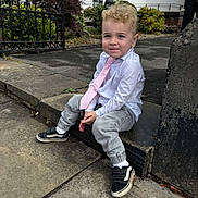 Mason is registered to the contest to win money with this photo: toddler, child, boy, sitting, concrete, sidewalk, tie, shirt, shoes, casual, outdoor, garden, greenery, gate, building, urban, portrait, curly_hair, smile, daylight