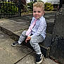 toddler, child, boy, sitting, concrete, sidewalk, tie, shirt, shoes, casual, outdoor, garden, greenery, gate, building, urban, portrait, curly_hair, smile, daylight