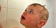Mason joined the competition — help win amazing prizes! toddler, child, wet, bathroom, shower, water, skin, face, curious, blue_eyes, hair, soap_holder, tiles, bath_time, expression, head, shoulder, adult_hand, water_droplets, indoor