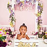 Ny'Ari is registered to the contest to win money with this photo: toddler, child, crate, flowers, floral_arch, butterflies, pink_background, portrait, cute, decor, baby, smiling, headband, white_clothing, wooden_crate, indoor, celebration, one, greenery, playful