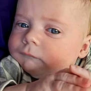 Jonathan is registered to the contest to win money with this photo: baby, infant, face, blue_eyes, chubby_cheeks, hand, close_up, portrait, newborn, skin, expression, ear, forehead, striped_clothing, indoor, wood_background, purple_blanket, gaze, calm, hands_clasped