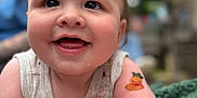 Wesley is registered to the contest to win money with this photo: baby, smiling, tattoo, arm, blanket, clothing, face, cheeks, person, infant, happy, skin, cute, outdoor, blurred_background, closeup, child, expression, holding, soft