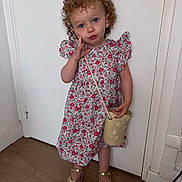 Amy a rejoint le concours — aidez-le/la à gagner de superbes lots ! blue_eyes, child, curly_hair, cute, door, dress, fashion, floral_pattern, hand_on_face, indoors, person, playful, pose, purse, sandals, smile, standing, toddler, wooden_floor, young_child