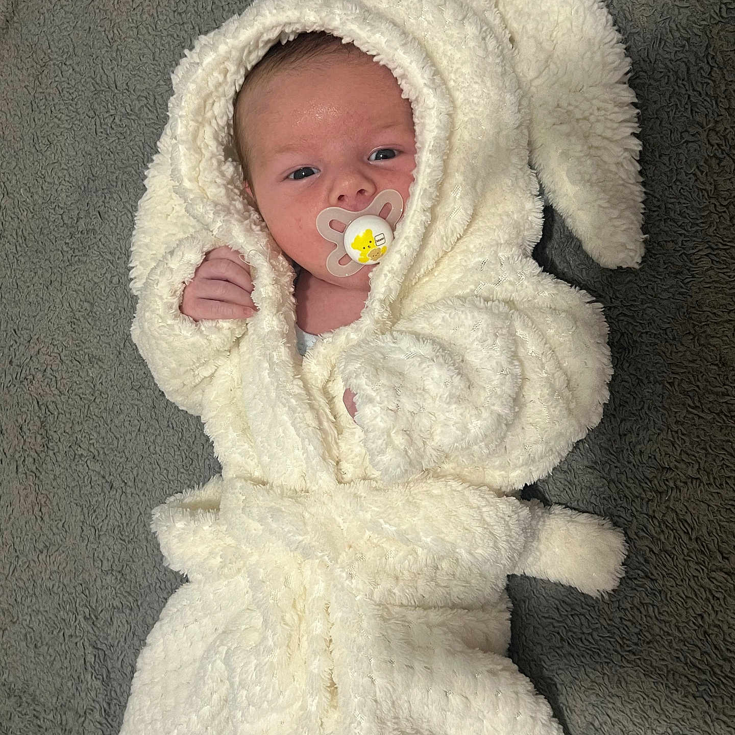 Denis joined the competition — help win amazing prizes! baby, bunny_ears, carpet, child, comfortable, cozy, cute, expression, face, fluffy, hood, indoor, infant, lying_down, newborn, pacifier, small_hands, soft_texture, wearing_clothes, white_robe