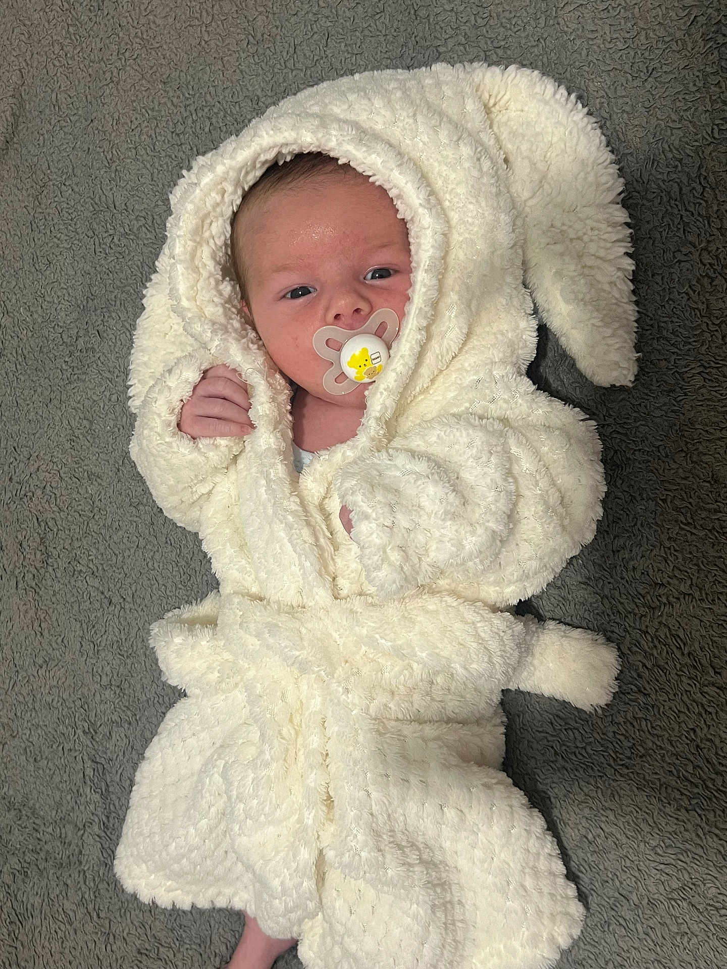 Denis joined the competition — help win amazing prizes! baby, infant, pacifier, white_robe, hood, bunny_ears, fluffy, soft_texture, carpet, lying_down, cute, cozy, newborn, child, small_hands, face, expression, indoor, comfortable, wearing_clothes