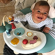 Nino a rejoint le concours — aidez-le/la à gagner de superbes lots ! baby, child, smiling, toy, activity_center, onesie, indoor, floor, blanket, happy, cute, infant, play, furniture, face, person, head, seat, colorful, toddler