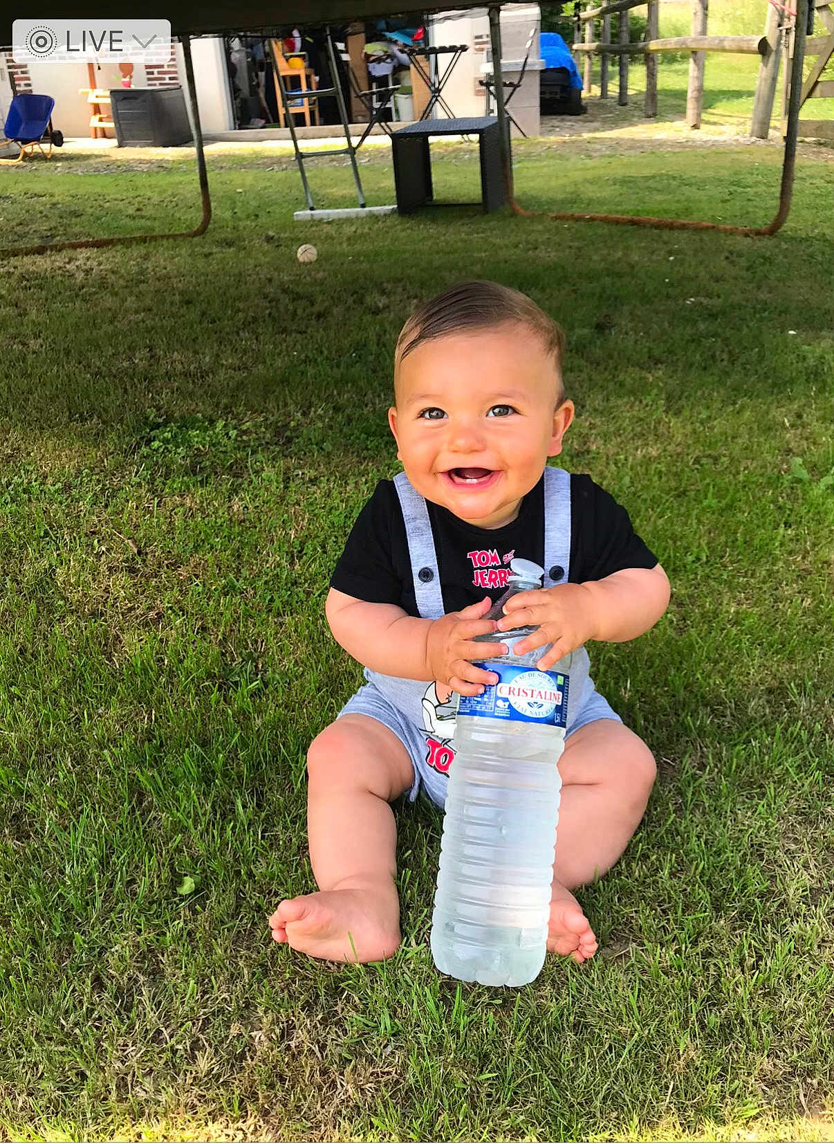 Nino participe au concours pour gagner de l'argent avec cette photo : baby, child, grass, outdoor, water_bottle, smiling, cute, sitting, clothing, barefoot, greenery, sunlight, happy, toy, playground, person, head, face, summer, nature
