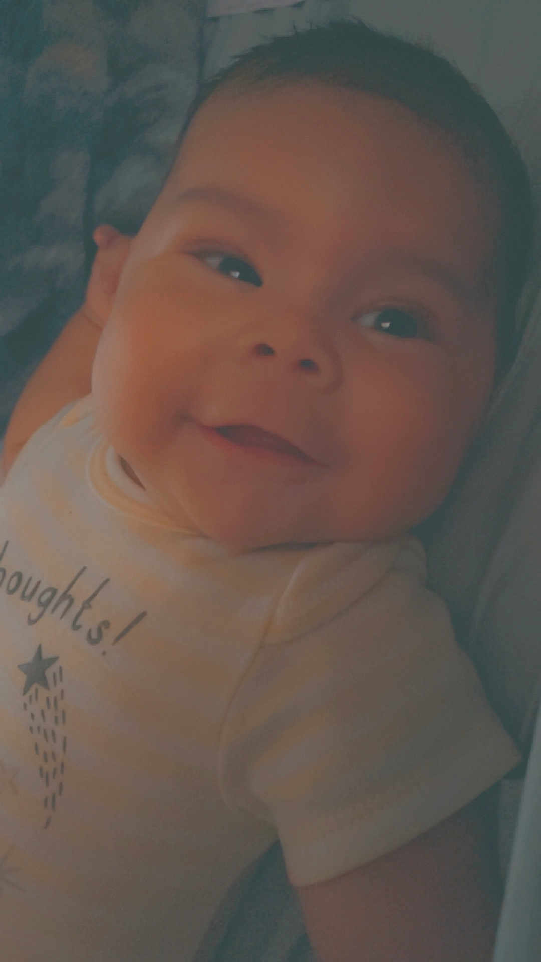 Liam joined the competition — help win amazing prizes! baby, smile, face, onesie, infant, child, portrait, closeup, cute, young, clothing, happy, skin, person, indoors, head, expression, babywear, lying_down, soft_light