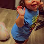 toddler, child, indoor, floor, wooden_floor, blue_tshirt, rolling_stones, shorts, purple_slippers, smiling, happy, curly_hair, pillow, rainbow_pattern, furniture, chair, playful, person, cute, standing