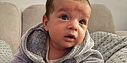 Chahine participe au concours pour gagner de l'argent avec cette photo : baby, child, infant, hooded_jacket, grey_clothing, cushion, patterned_fabric, stars, moons, indoor, sofa, cozy, curious, face, hands, portrait, expression, young, resting, cute