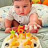 baby, balloon, birthday_candle, blueberry, cake, celebration, closeup, cream, cute, fruit, indoor, infant, messy_hand, number_candle, orange_balloon, orange_candle, quilt, star_candle, striped_shirt, yellow_candle