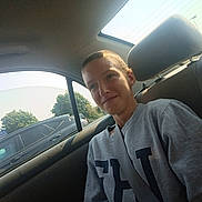 Mikel joined the competition — help win amazing prizes! person, teenager, car_interior, seatbelt, window, daylight, parking_lot, sign, goodwill, casual_clothing, short_hair, gray_sweatshirt, backseat, automobile, outdoor, trees, vehicle, seated, portrait, smile