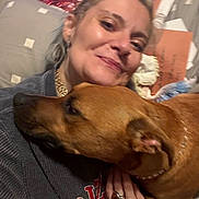 Bear is registered to the contest to win money with this photo: affection, bed, blanket, brown_dog, casual, closeup, clothing, cuddle, dog, earring, face, hand, human, indoor, jewelry, person, pet, pillow, ring, smile