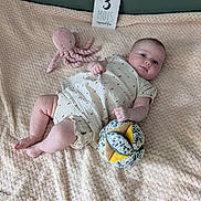 Norah participe au concours pour gagner de l'argent avec cette photo : baby, infant, blanket, plush_toy, octopus_toy, fabric_ball, card, milestone_card, clothing, cute, lying_down, indoor, soft_texture, patterned_outfit, child, adorable, baby_girl, skin, head, face