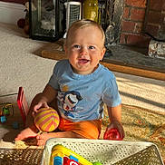 Spencer is registered to the contest to win money with this photo: toddler, child, smiling, indoor, carpet, toy, basket, colorful, fireplace, brick, shirt, orange_shorts, happy, person, foot, playtime, home, light, shadow, living_room