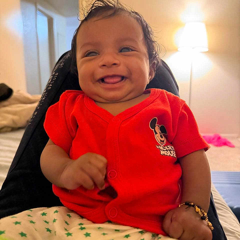 Sahasra joined the competition — help win amazing prizes! baby, bedroom, bracelet, child, clothing, cute, happy, home, indoor, infant, lamp, mickey_mouse, person, portrait, red_shirt, shorts, sitting, smiling, star_pattern, young_child