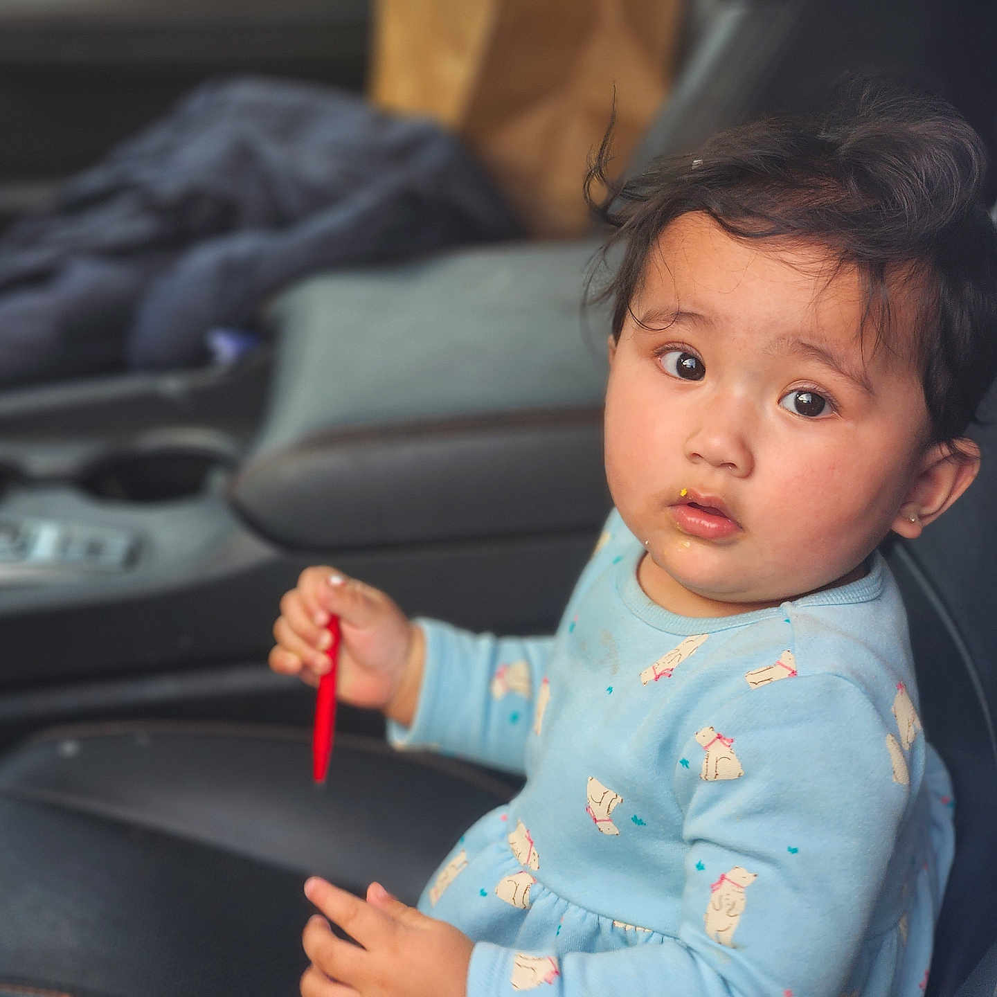 Dityaa joined the competition — help win amazing prizes! child, toddler, baby, portrait, car, car_interior, seated, face, eyes, curious, serious_expression, dark_hair, blue_clothing, patterned_clothing, puppy_pattern, snack, red_object, seat, seatbelt_area, indoor
