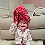 baby, carpet, child, clothing, comfort, cute, expression, face, furniture, happy, headwear, indoor, infant, living_room, playful, robe, sitting, skin, smiling, towel