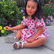 Aitana is registered to the contest to win money with this photo: cherry_pattern, child, colorful, dress, flowers, garden, girl, nature, outdoor, patio, plants, portrait, portrait_photography, sandals, sitting, smiling, toddler, white_bow, wooden_fence, yellow_flower