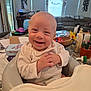 Ares is registered to the contest to win money with this photo: baby, smiling, high_chair, indoor, happy, person, infant, clothing, table, furniture, face, hands, living_room, birthday, decorations, toy, household, home, cute, child