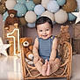 baby, child, smiling, wicker_chair, teddy_bear, balloons, birthday, number_one, star_lights, decorations, blue_outfit, cute, indoor, celebration, happy, infant, portrait, festive, soft_lighting, floor