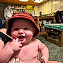 Parker is registered to the contest to win money with this photo: baby, bucket_hat, carpet, child, cute, diaper, finger_in_mouth, furniture, hand, happy, hat, human, indoor, kitchen, living_room, person, skin, smiling, tattoo, wooden_ceiling