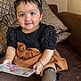 toddler, child, smile, book, couch, brown_skirt, black_top, headband, bow, fishnet_stockings, cushion, indoor, happy, portrait, sitting, clothing, person, furniture, cute, baby