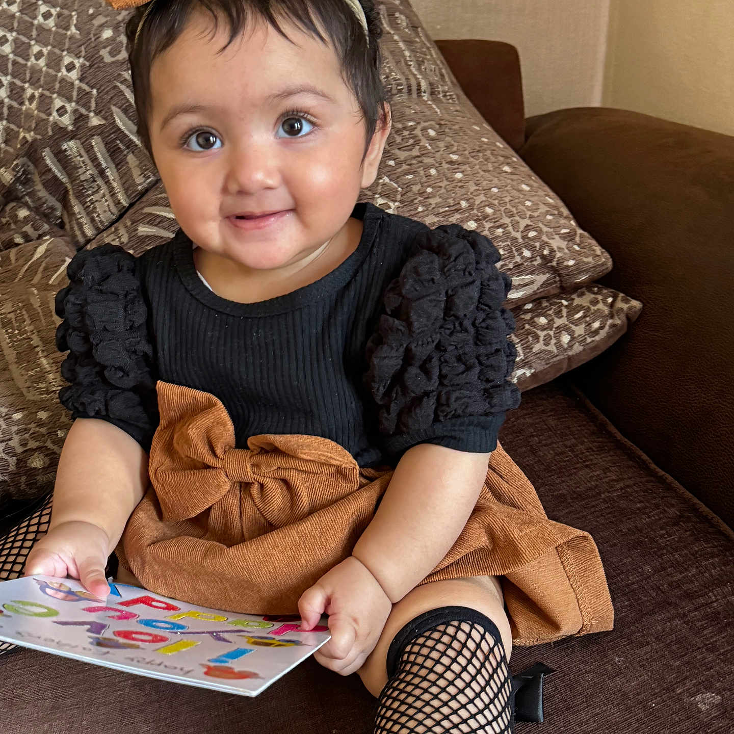 Anushay joined the competition — help win amazing prizes! baby, black_top, book, bow, brown_skirt, child, clothing, couch, cushion, cute, fishnet_stockings, furniture, happy, headband, indoor, person, portrait, sitting, smile, toddler