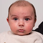 Maé a rejoint le concours — aidez-le/la à gagner de superbes lots ! baby, portrait, face, expression, sweater, clothing, textile, embroidered_text, curious, wide_eyes, indoor, neutral_background, close_up, child, person, skin, head, eyebrows, cute, newborn