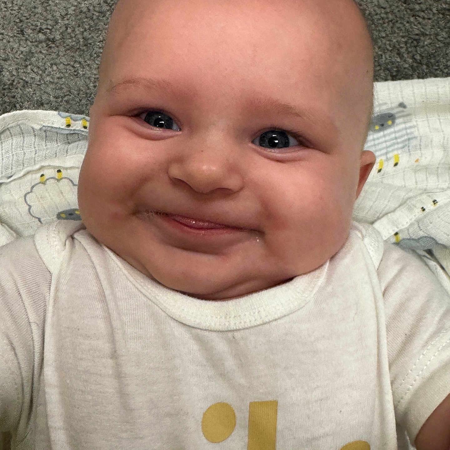 Maylynn is registered to the contest to win money with this photo: baby, blanket, carpet, cheeks, child, closeup, clothing, cute, eyes, face, happy, infant, logo, lying_down, nike, person, portrait, skin, smiling, white_shirt