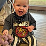 baby, band_tshirt, child, clothing, cute, expression, face, floor, foo_fighters_tshirt, hand, happy, head, indoor, infant, person, plush_toy, sitting, smiling, striped_pants, toy