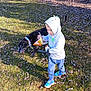black_dog, blue_shoes, casual_clothing, child, daytime, dog, fun, grass, hoodie, leash, leaves, nature, outdoor, person, pet, playful, snack_bag, sunlight, trees, walking