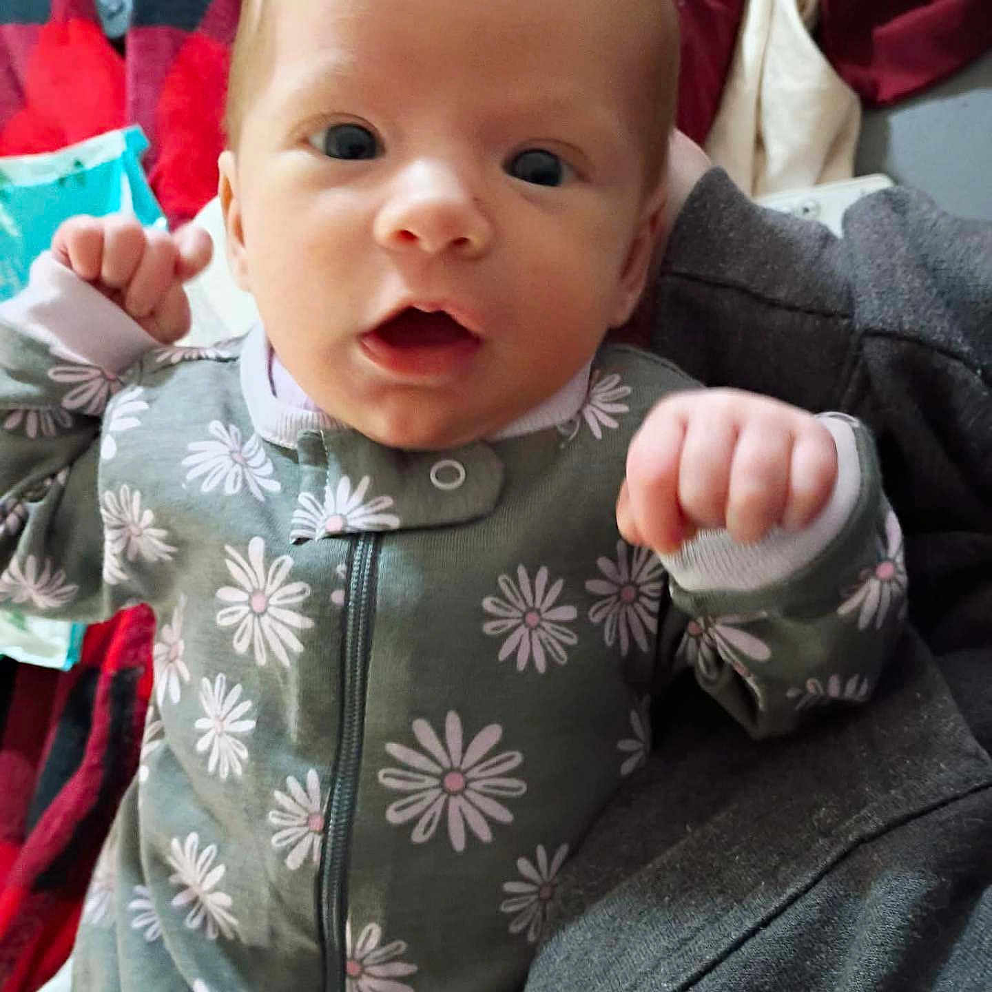 Khaos joined the competition — help win amazing prizes! baby, bedding, blanket, closeup, clothing, daisy_pattern, expression, eyes, face, fists, hands, head, indoor, infant, lying_down, newborn, onesie, portrait, remote_control, skin