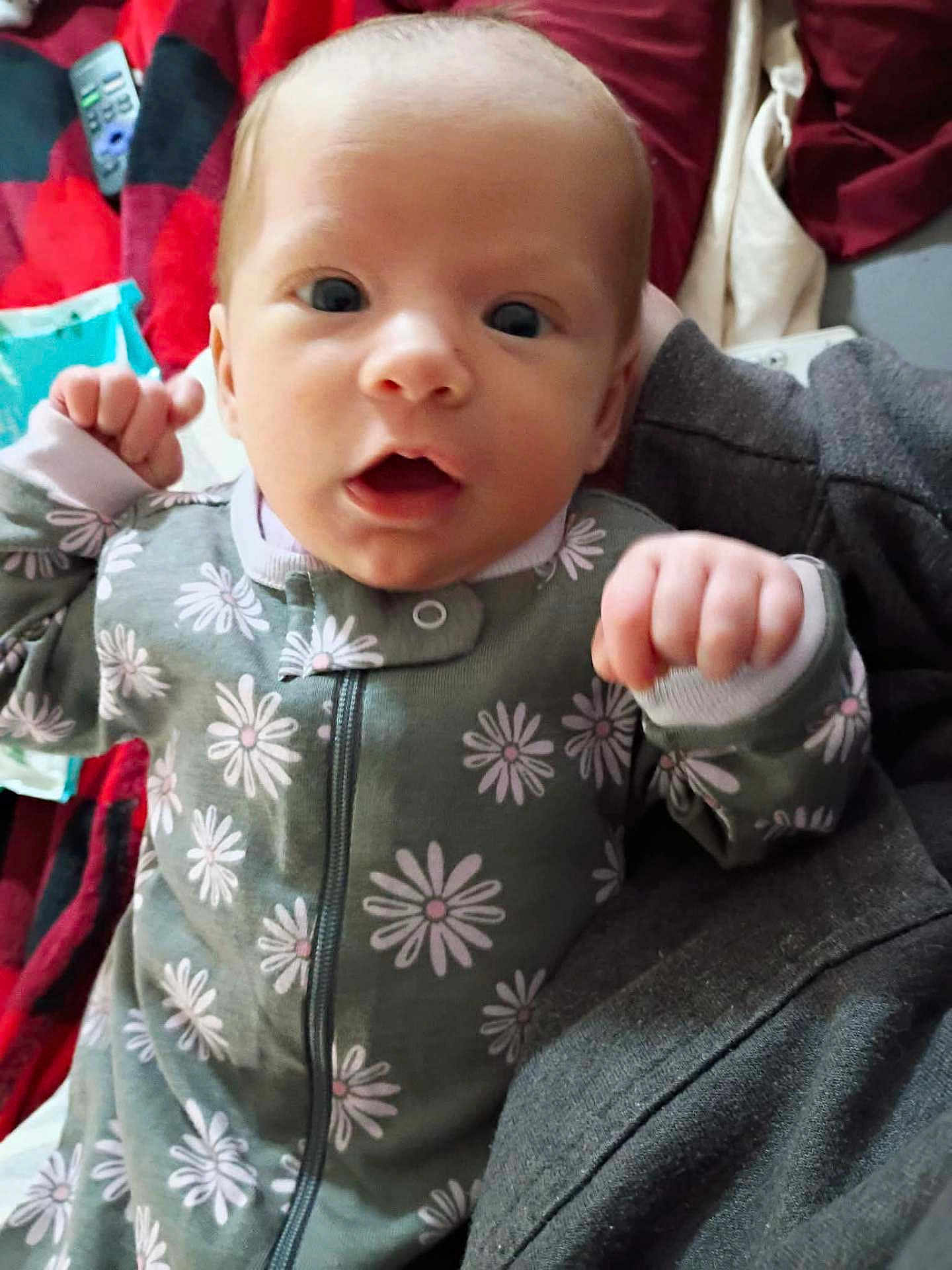 Khaos joined the competition — help win amazing prizes! baby, newborn, infant, onesie, daisy_pattern, face, closeup, eyes, hands, fists, portrait, indoor, blanket, bedding, remote_control, clothing, expression, skin, head, lying_down