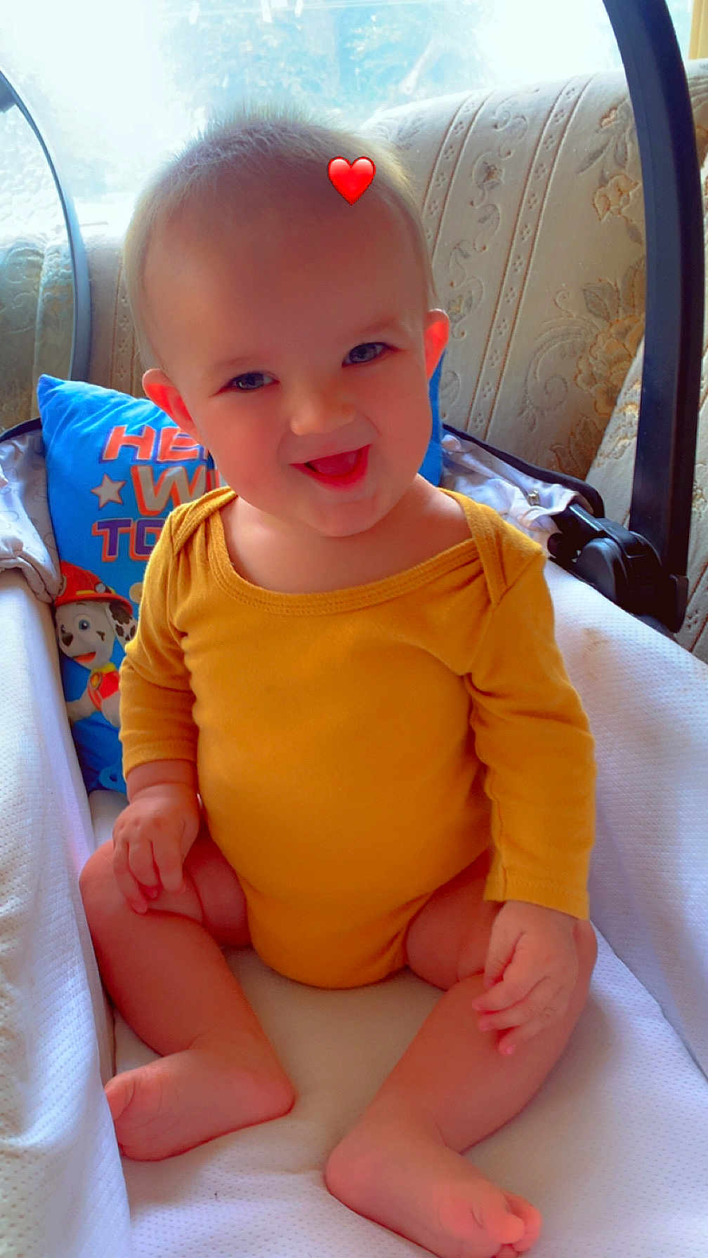Alonzo participe au concours pour gagner de l'argent avec cette photo : baby, child, smiling, yellow_clothing, onesie, sitting, infant_seat, pillow, cartoon, heart_emoji, indoors, cozy, cute, happy, face, skin, foot, hand, window, soft_light