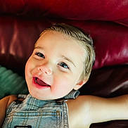 Kai joined the competition — help win amazing prizes! child, toddler, smile, happy, face, denim_overalls, clothing, blue_eyes, skin, hair, leather_couch, red, indoor, portrait, baby, cute, young, person, relaxing, closeup