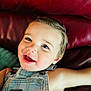 child, toddler, smile, happy, face, denim_overalls, clothing, blue_eyes, skin, hair, leather_couch, red, indoor, portrait, baby, cute, young, person, relaxing, closeup