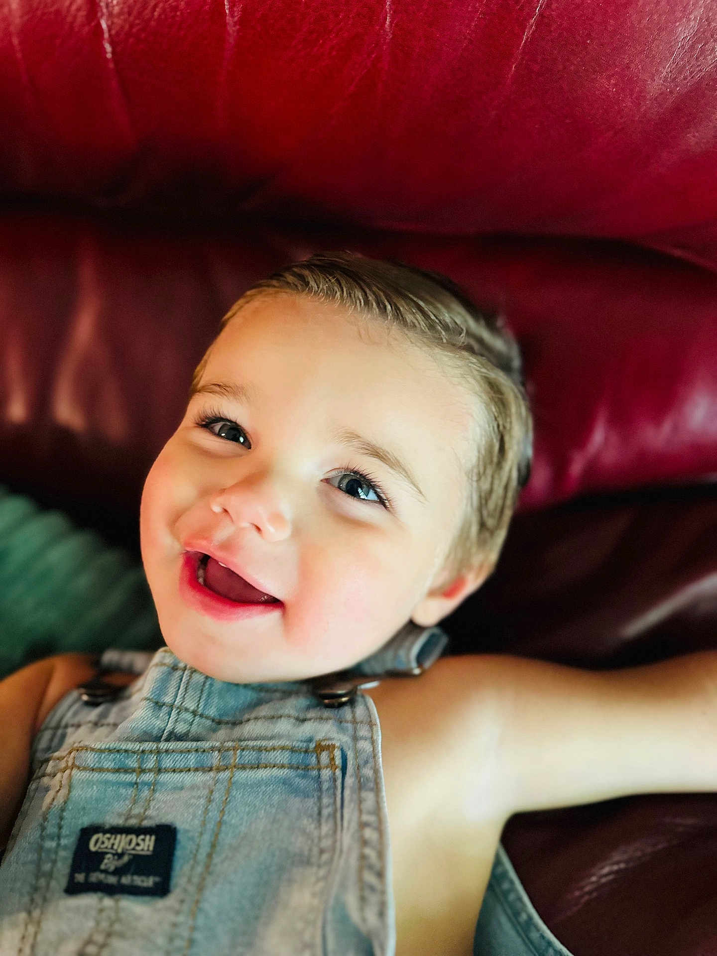 Kai joined the competition — help win amazing prizes! child, toddler, smile, happy, face, denim_overalls, clothing, blue_eyes, skin, hair, leather_couch, red, indoor, portrait, baby, cute, young, person, relaxing, closeup