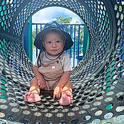 Jasper is registered to the contest to win money with this photo: toddler, child, playground, hat, overalls, sitting, tunnel, sunlight, shadows, outdoor, play, baby, cute, smiling, feet, clothing, daylight, metal, pattern, fun