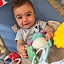 baby, child, toy, blanket, smiling, face, hand, blue, yellow, red, plush_toy, play, infant, cute, lying_down, striped_shirt, indoor, closeup, happy, person