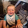 baby, smiling, stroller, indoor, child, happy, face, hand, blue_shirt, bib, grip, seat, plant, home, decor, furniture, person, cute, infant, portrait