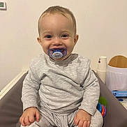 Matéo participe au concours pour gagner de l'argent avec cette photo : toddler, child, pacifier, smile, grey_clothing, sitting, indoor, happy, baby, pajamas, hands, face, toy, home, expression, young_child, comfort, casual, blank_wall, person